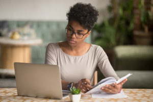 woman-reading-a-book-and-using-a-laptop