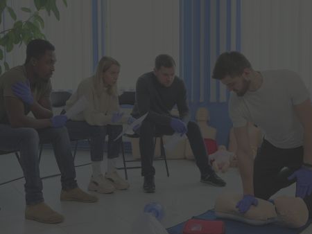 Group of students participating in a CPR class, watching an instructor perform chest compressions on a mannequin.