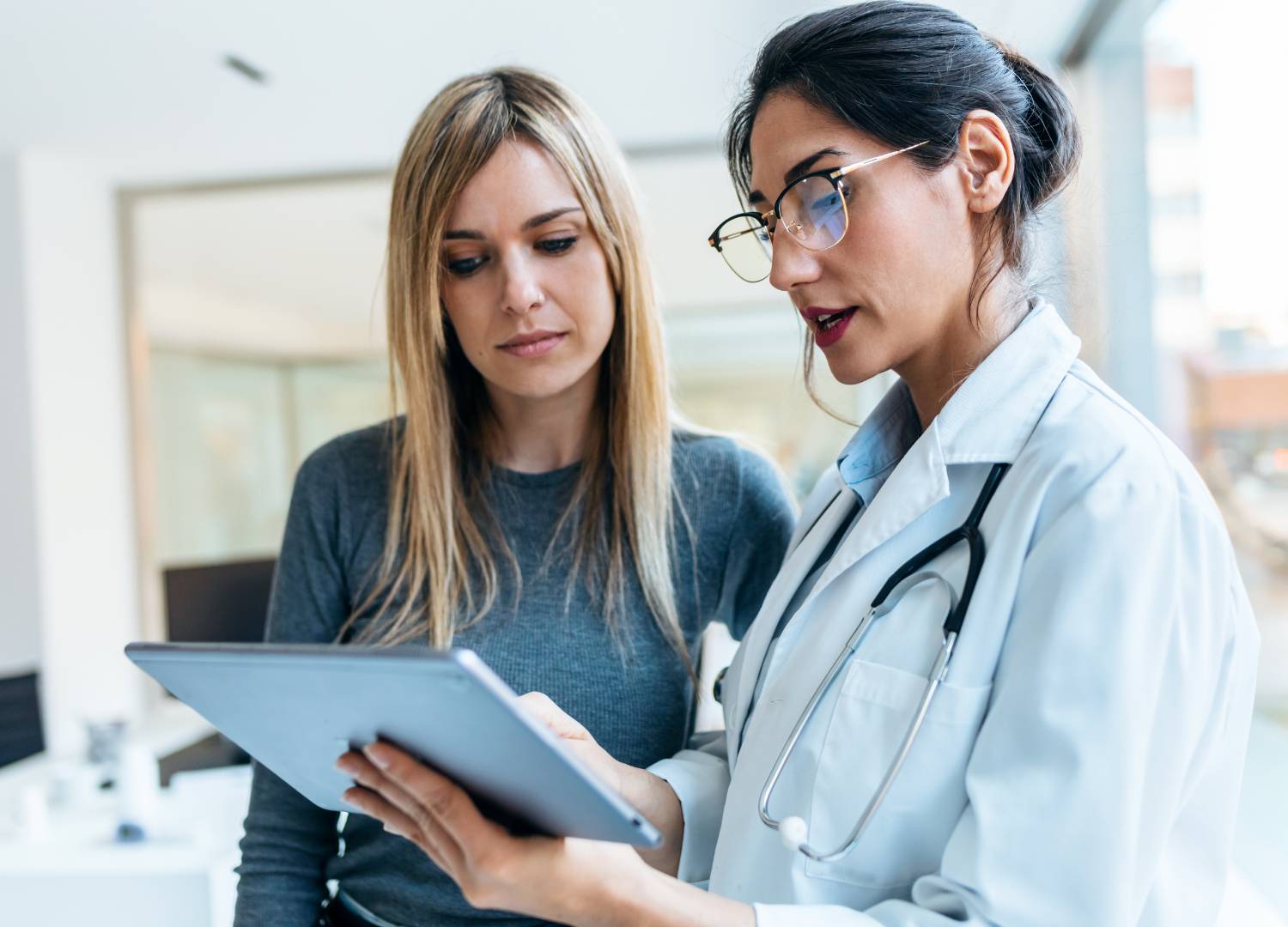 A female doctor with glasses consulting a patient, showing information on a tablet. 