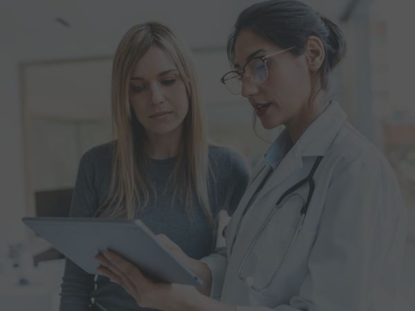 A female doctor with glasses consulting a patient, showing information on a tablet.